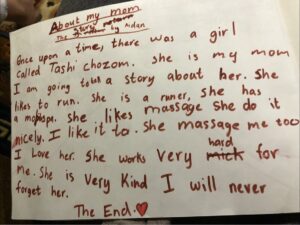 Ein Papier mit kindlicher Handschrift. Abgebildet ist ein Aufsatz der 8-jährigen Tochter von Tashi, die mit Liebe und Stolz ihre Mutter beschreibt. Einige Wörter sind durchgestrichen und überschrieben. Aidan ist seit 2020 in der Schule.