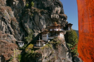 A temple complex built on the protrusions of a steep, high rock mass. The temple shines in the sun with its white facade, red and gold frieze under a pagoda roof.